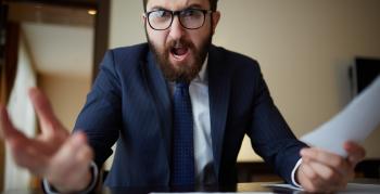 Angry boss wearing glasses in a business suit sitting at desk