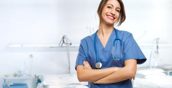 A caucasian woman smiling with her hands folded. She is wearing scrubs and is a medical assitant