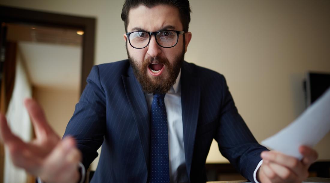 Angry boss wearing glasses in a business suit sitting at desk