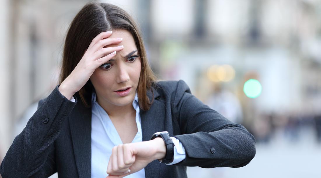 Front view of a worried business woman checking time on her smart watch on a city street.