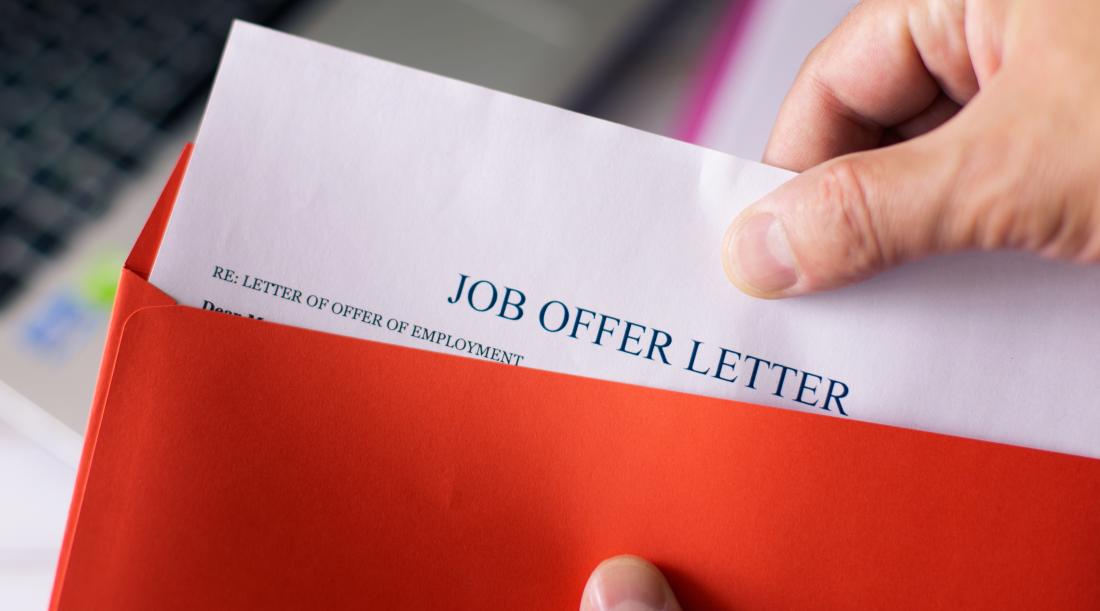 A man's hand pulling out a job offer letter out of a red folder.