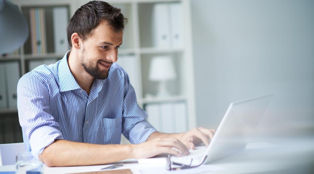 A man smiling while working in front of his laptop.